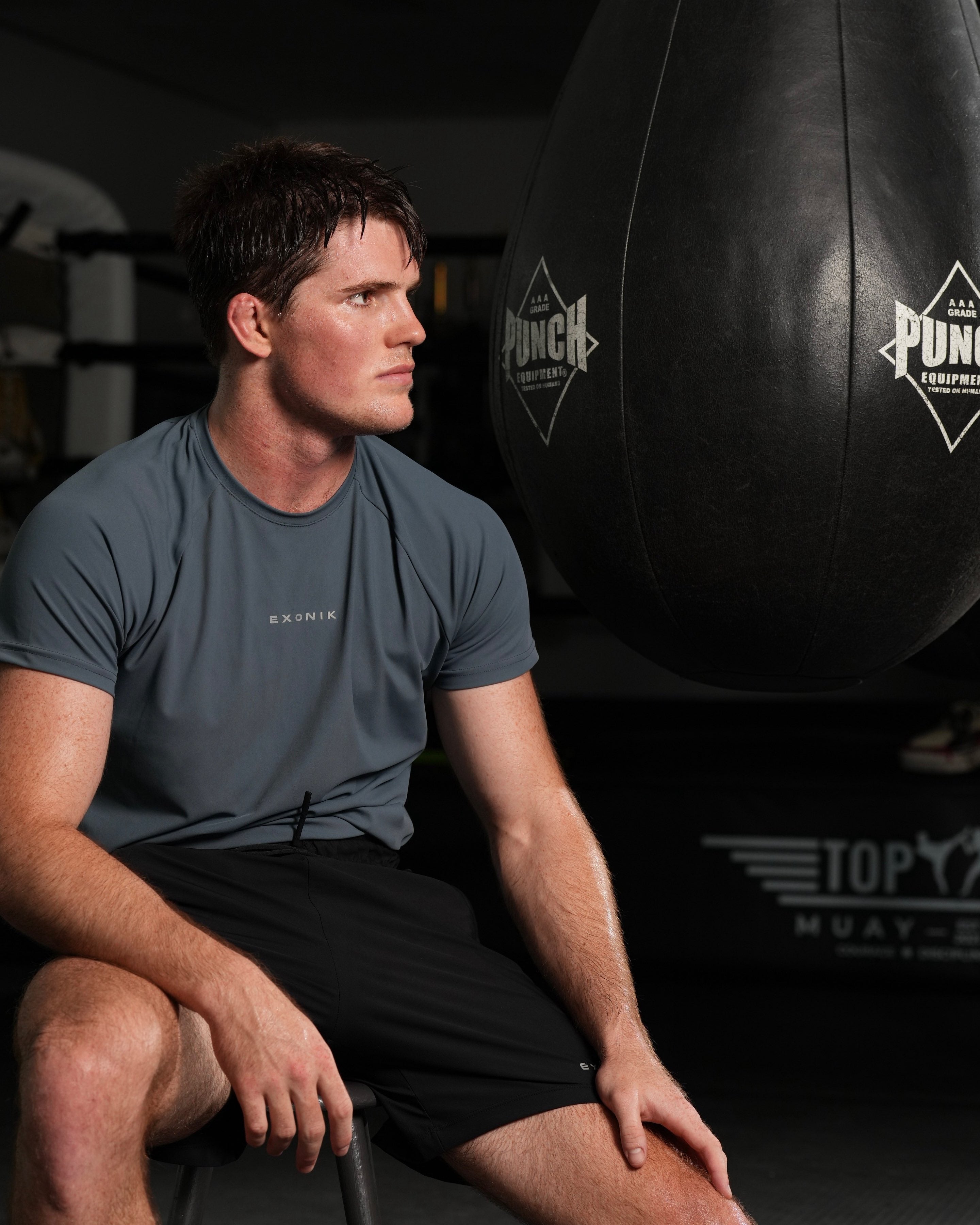 Close shot full-body  side view of a male model wearing the Exonik Systema Tee in Basalt Grey in a studio setting.