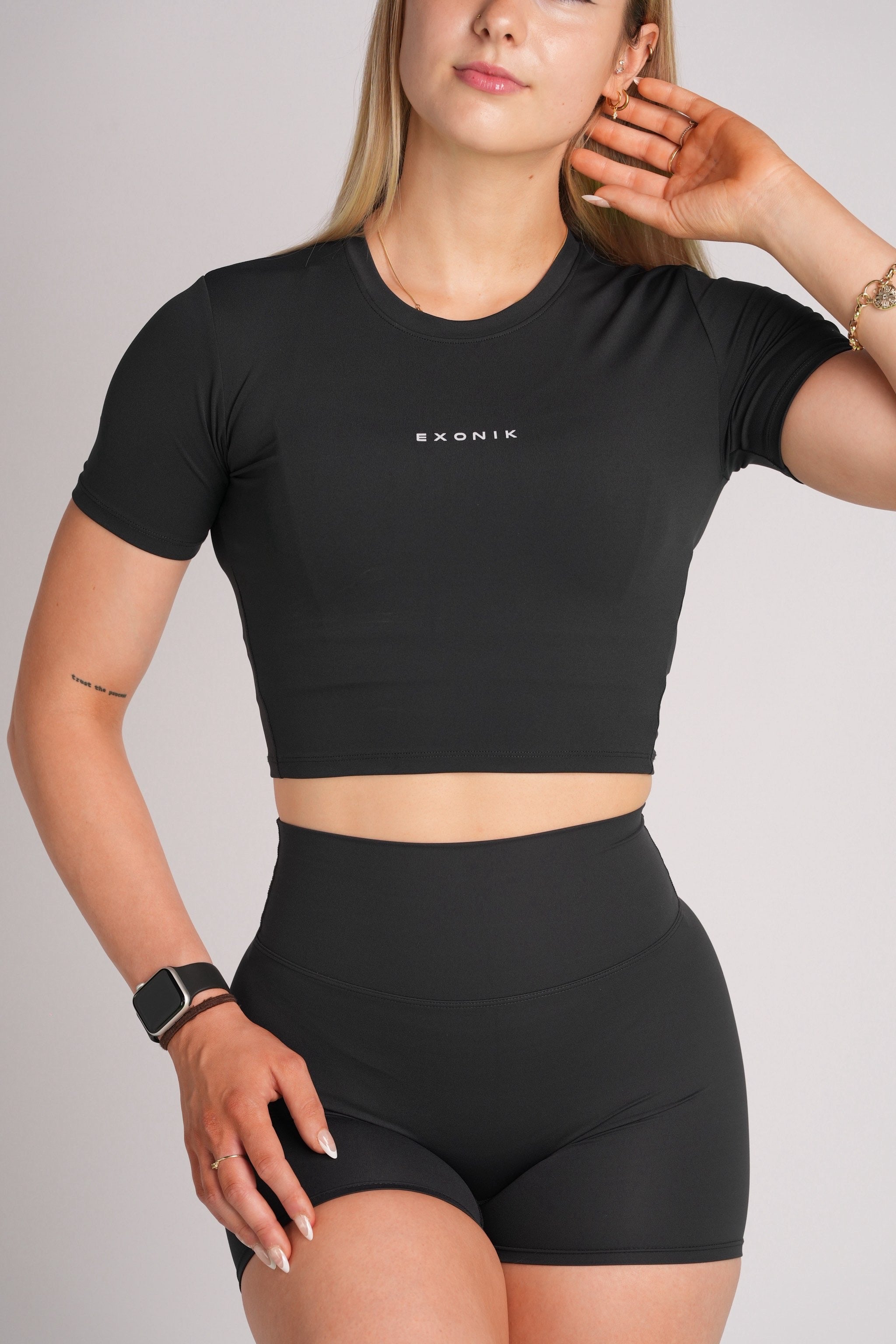 Half-body front view of a model wearing the Exonik ExoTech Liberty Crop Tee in Black in a studio setting.