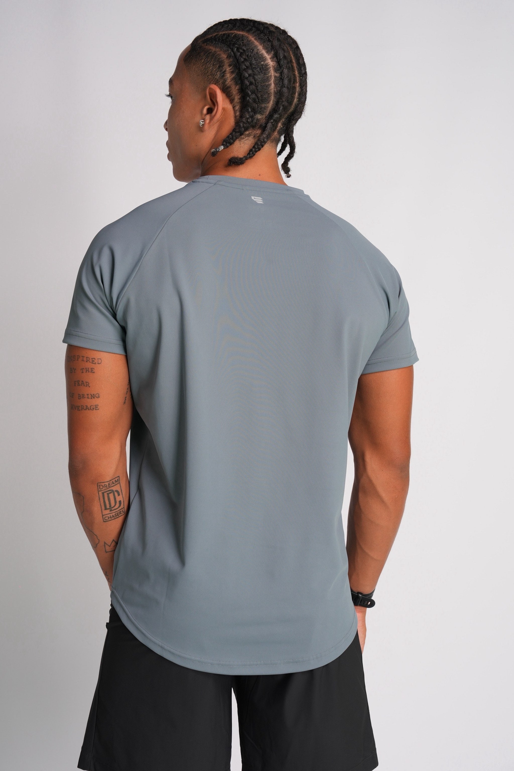 Half-body back view of a male model wearing the Exonik Systema Tee in Basalt Grey in a studio setting.