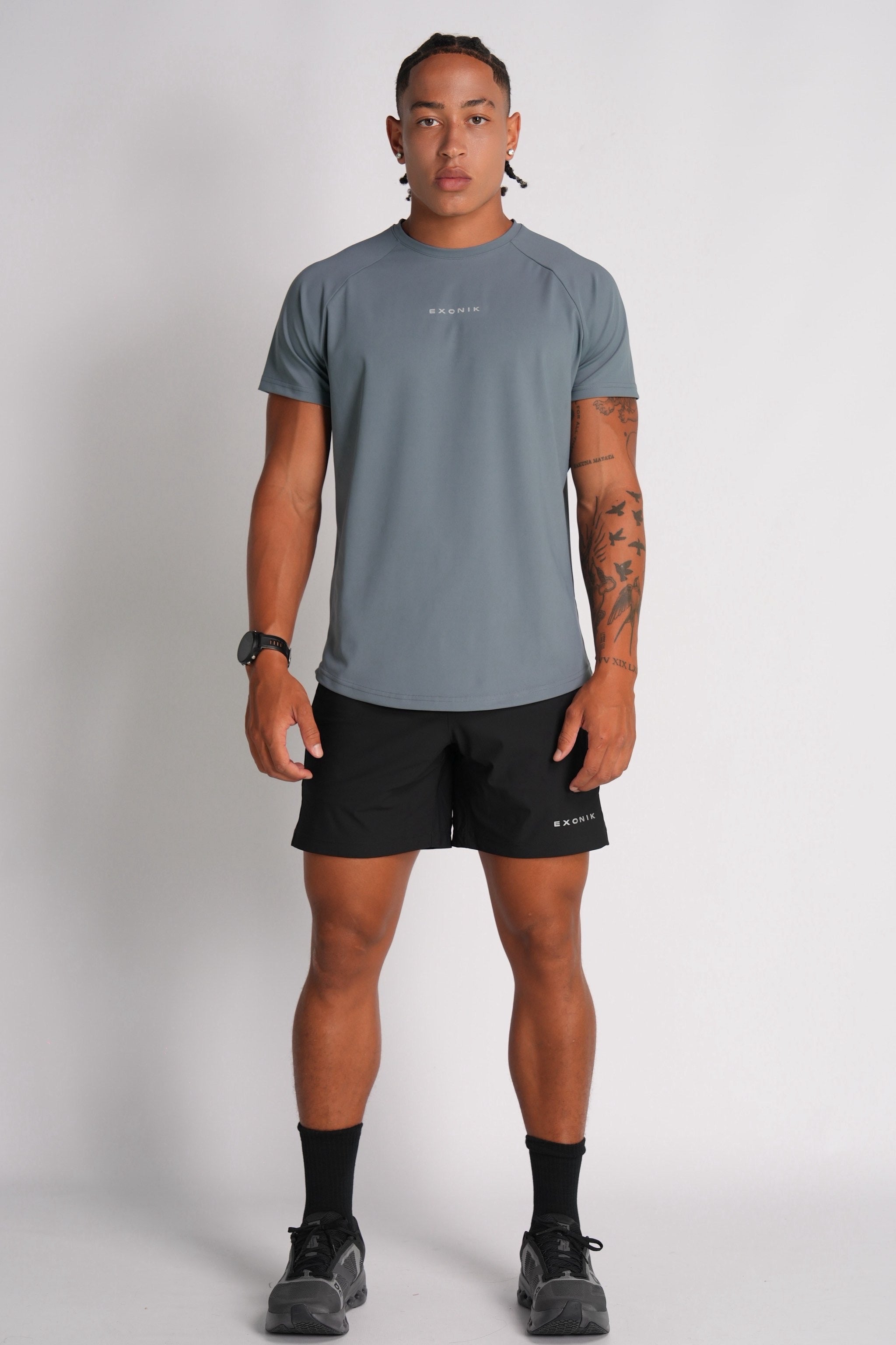Full-body front view of a male model wearing the Exonik Systema Tee in Basalt Grey in a studio setting.