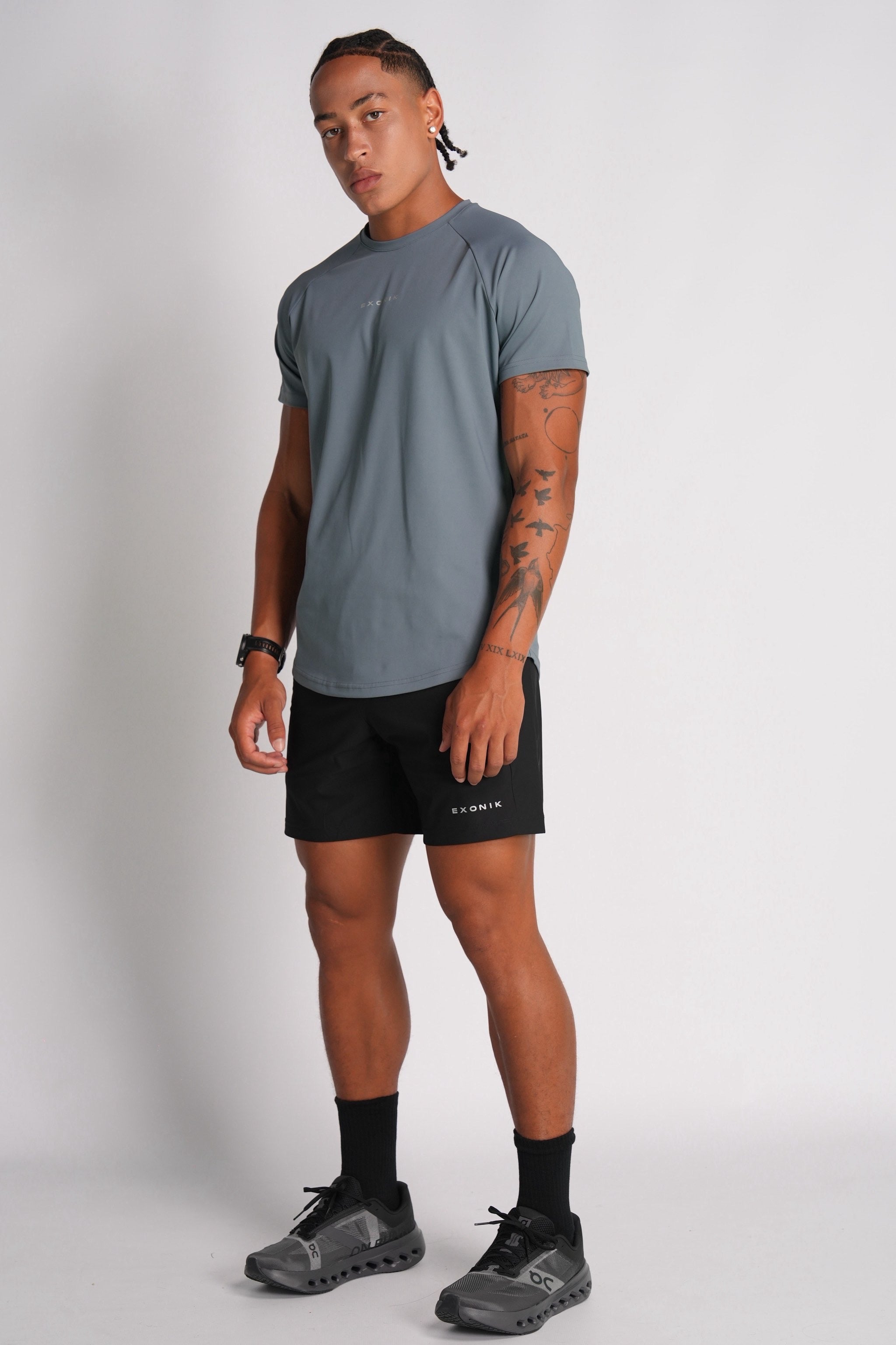 Full-body side view of a male model wearing the Exonik Systema Tee in Basalt Grey in a studio setting.