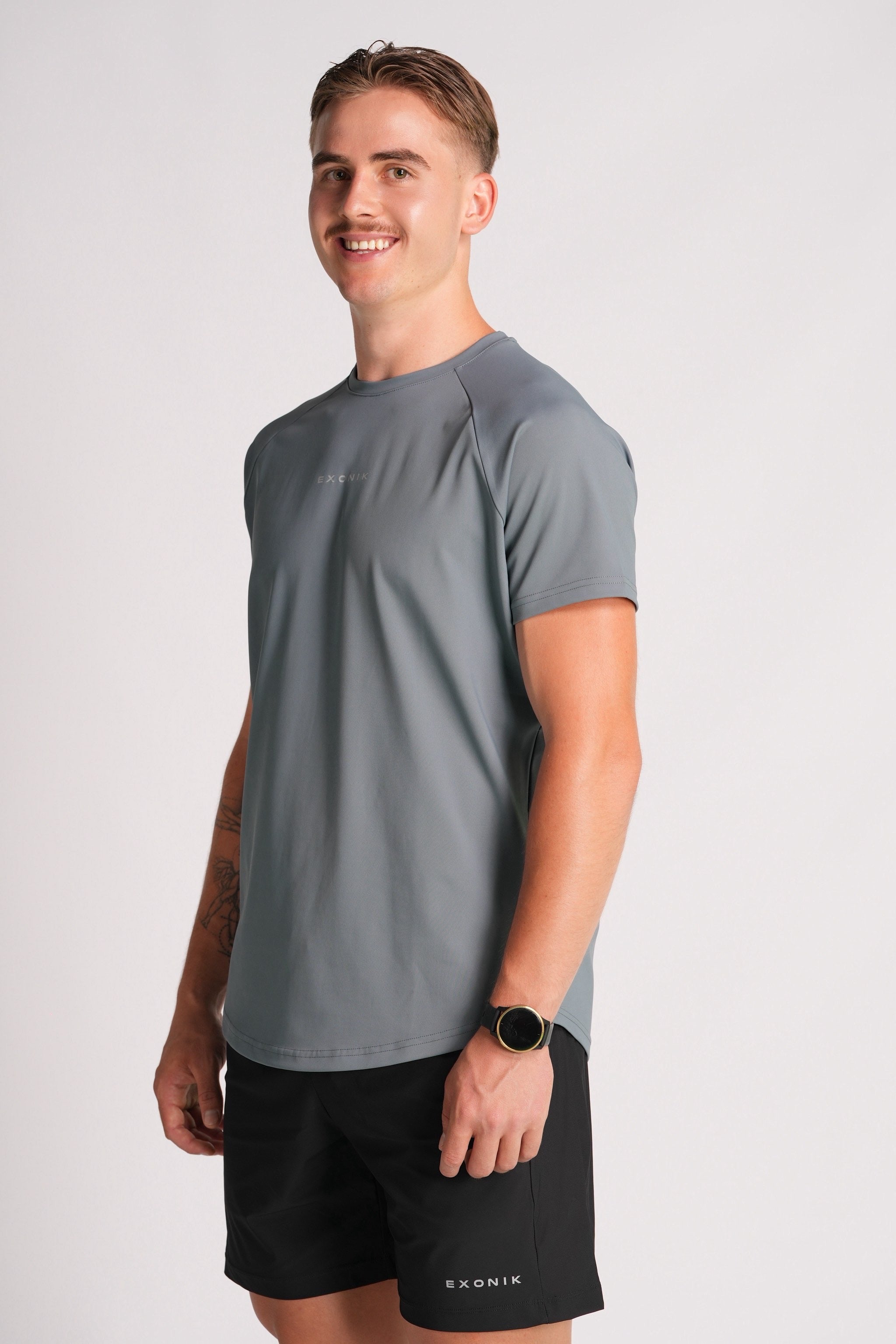 Close shot full-body  side view of a male model wearing the Exonik Systema Tee in Basalt Grey in a studio setting.