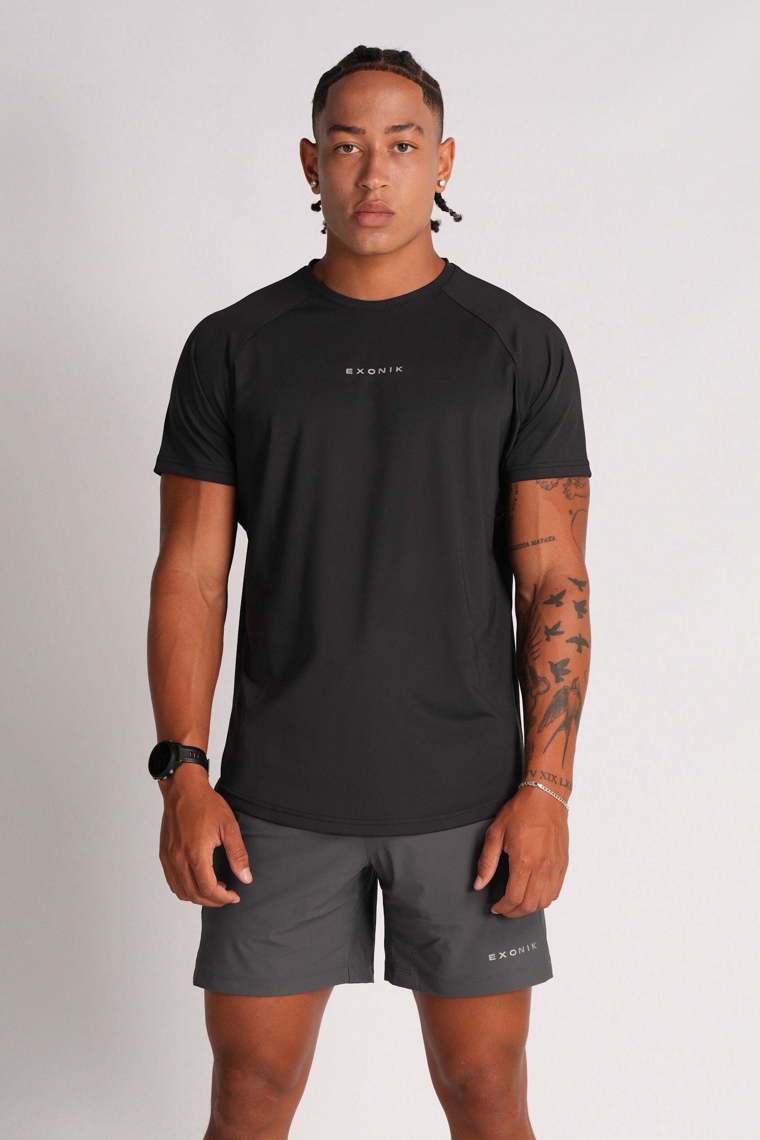 Full-body front view of a male model wearing the Exonik Systema Tee in Black in a studio setting.