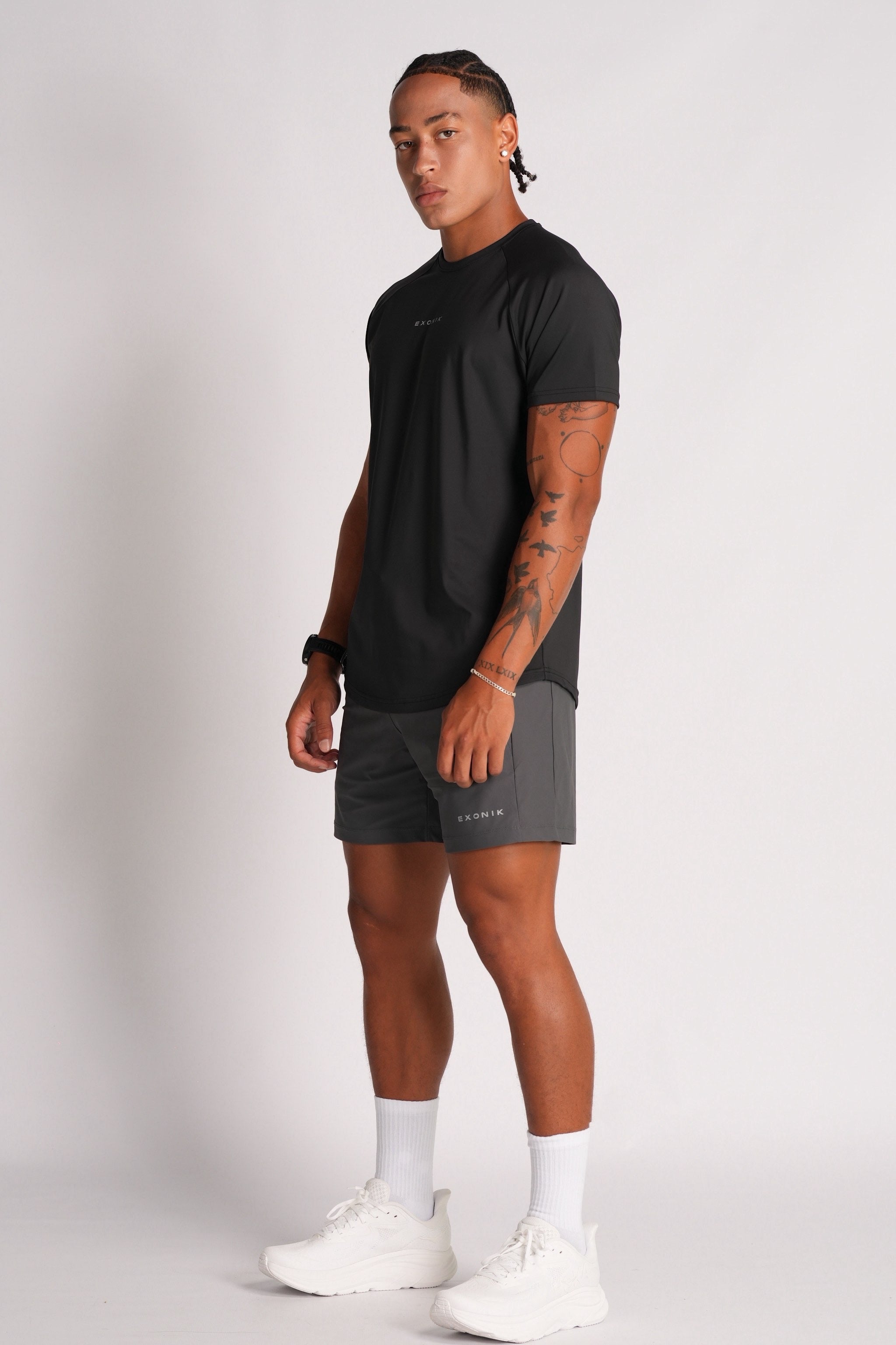 Full-body side view of a male model wearing the Exonik Systema Tee in Black in a studio setting.